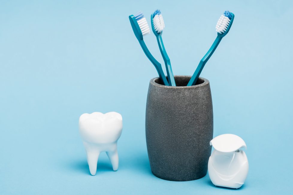 tre blå tandbørster i et krus med to tænder neden for på blå baggrund