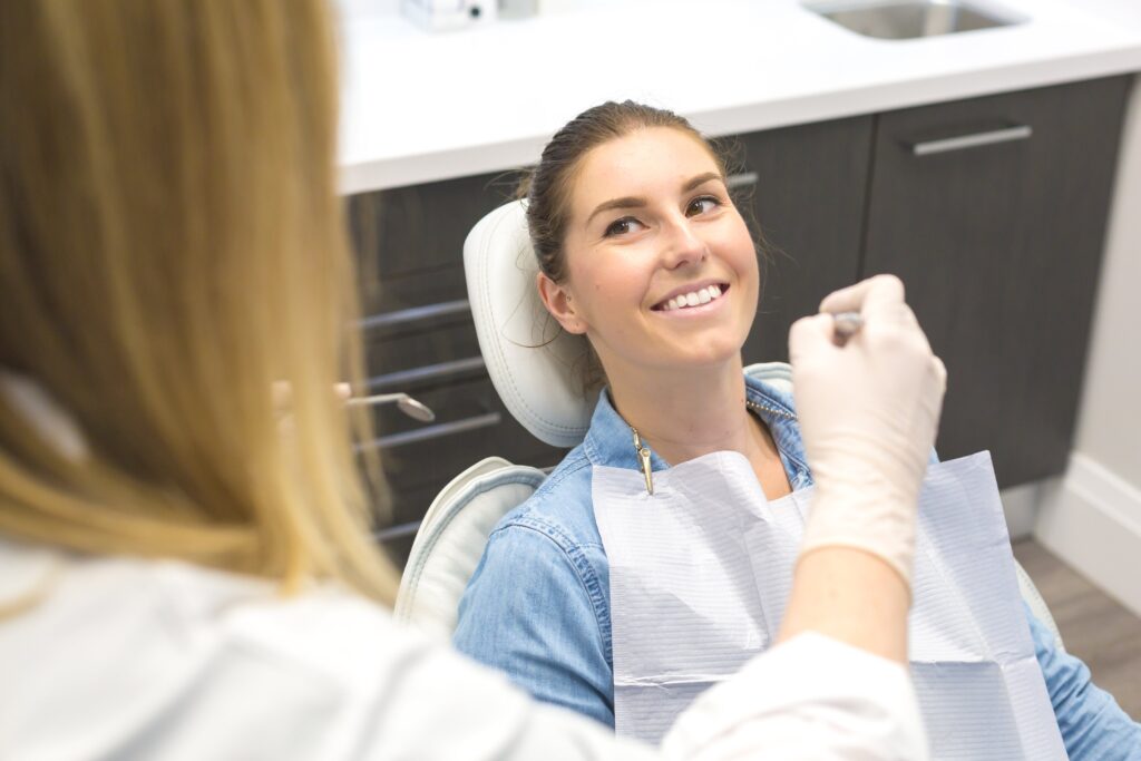 billede taget over skulderen af en tandlæge med hvide handsker. tandlægen står over en smilende kvindelig patient