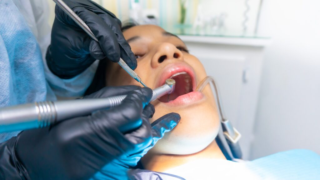 Nærbillede af en kvinde, som er til tandlæge. Hendes mund er åben, og tandlægen er i gang.